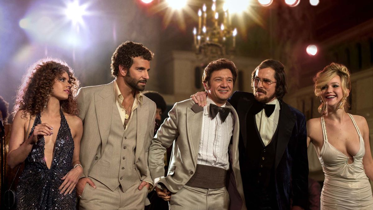 Three men and two women walk down the street in formal wear while fireworks go off behind them in American Hustle