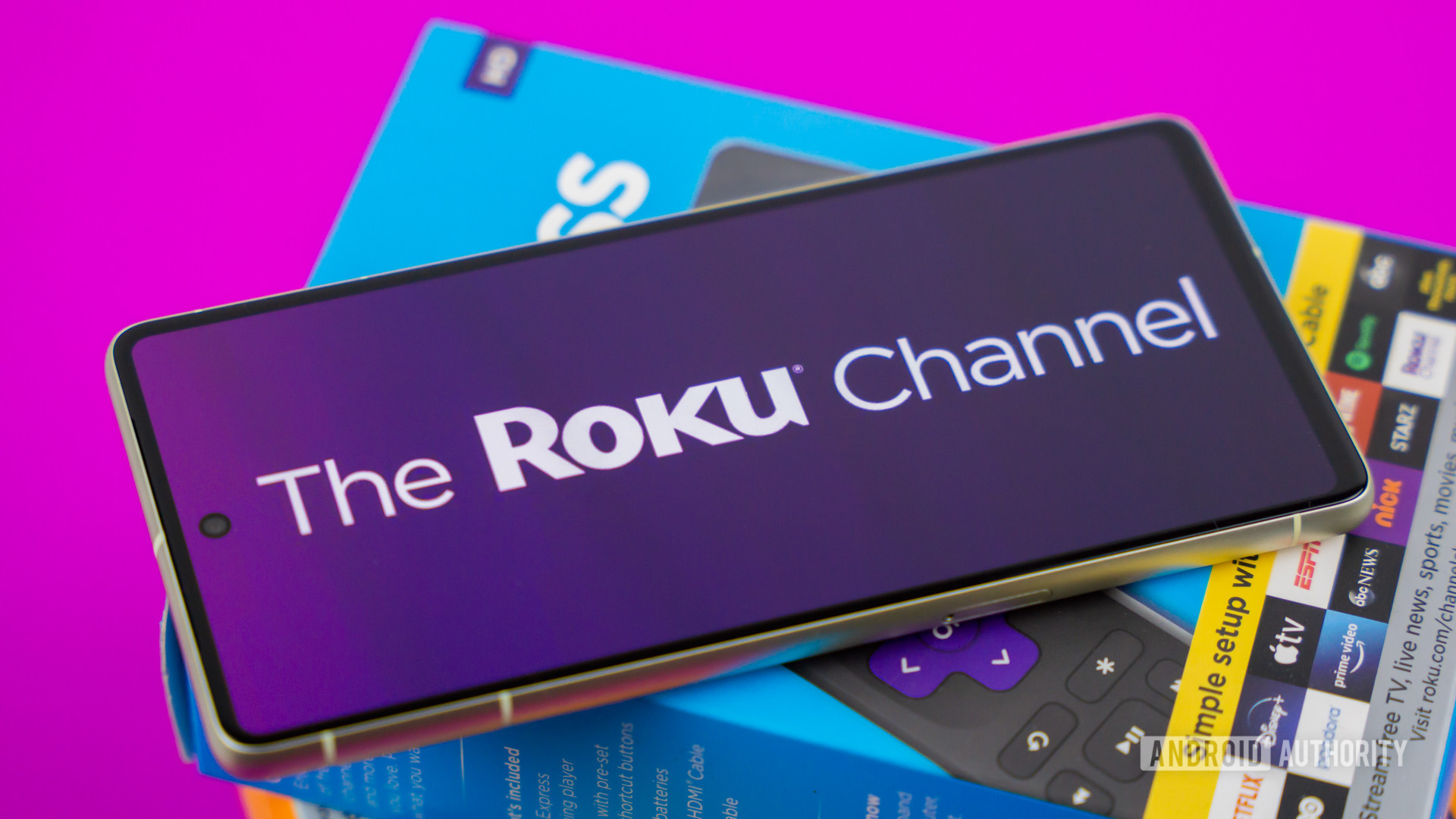 Stock photo of The Roku Channel logo on phone next to Roku boxes 4