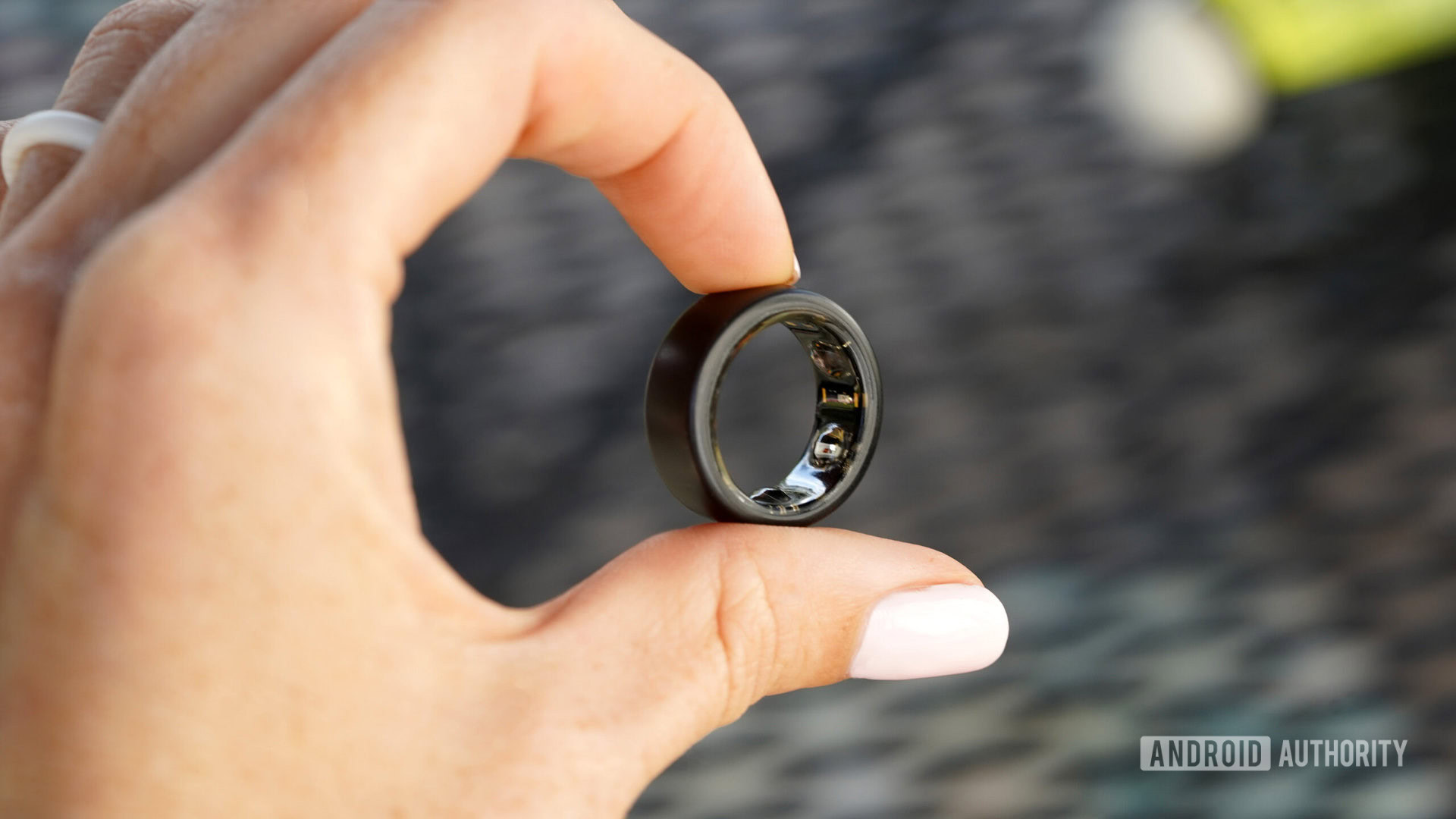 Un usuario sostiene un Oura Ring 3 entre dos dedos, mostrando los sensores del dispositivo.