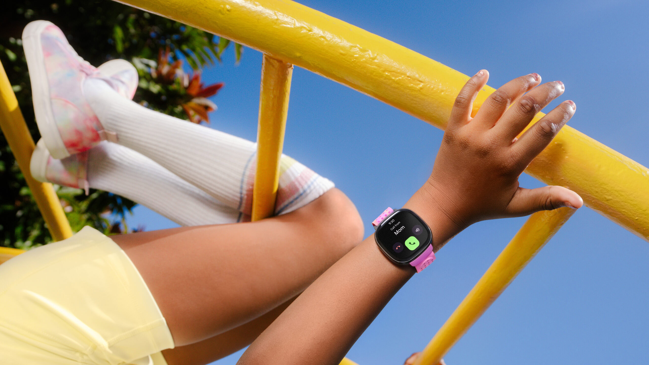 A child wearing a Fitbit Ace LTE hangs from a piece of playground equipment.