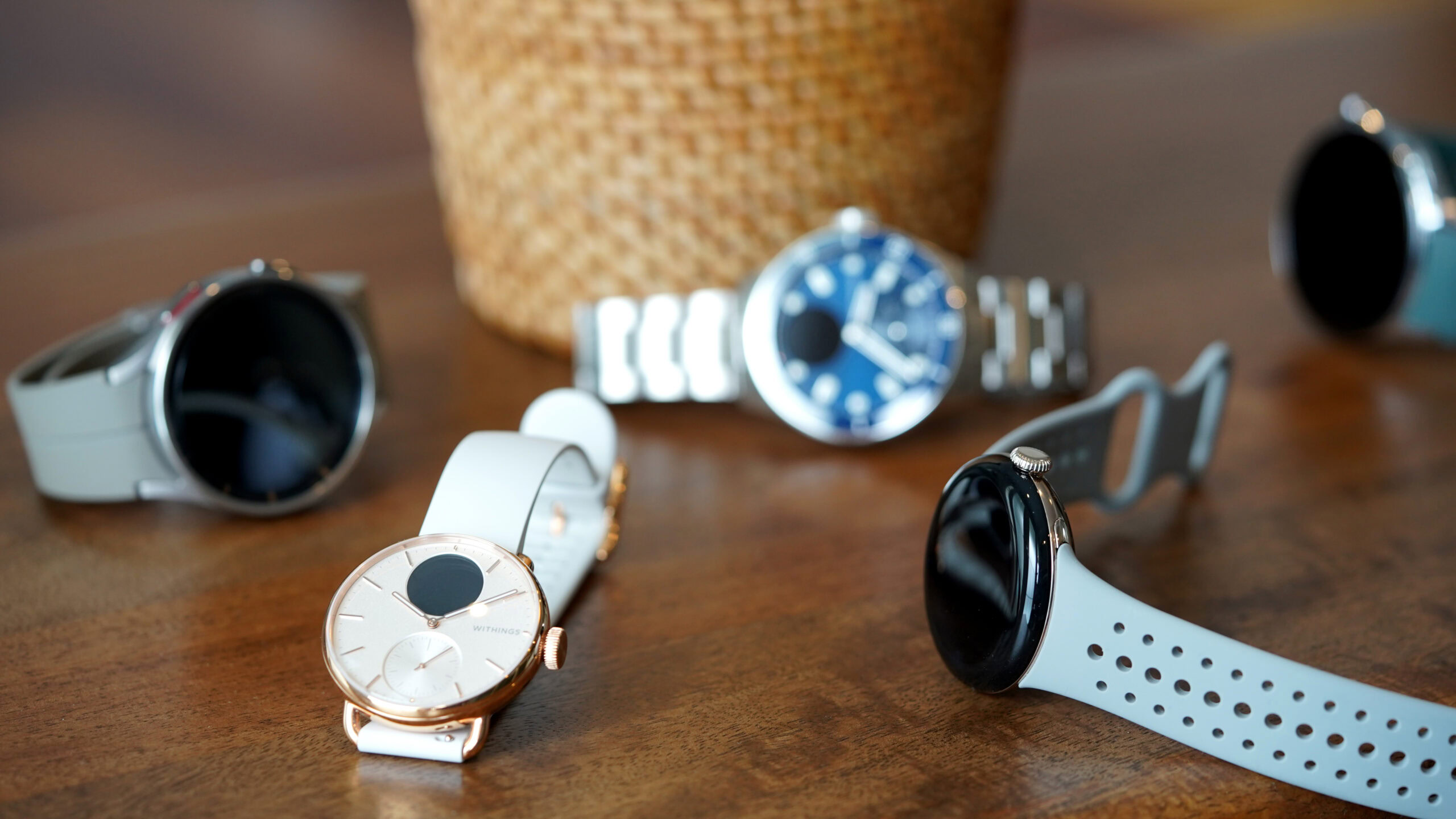 A variety of smartwatches and hybrid devices rest on a wooden surface.