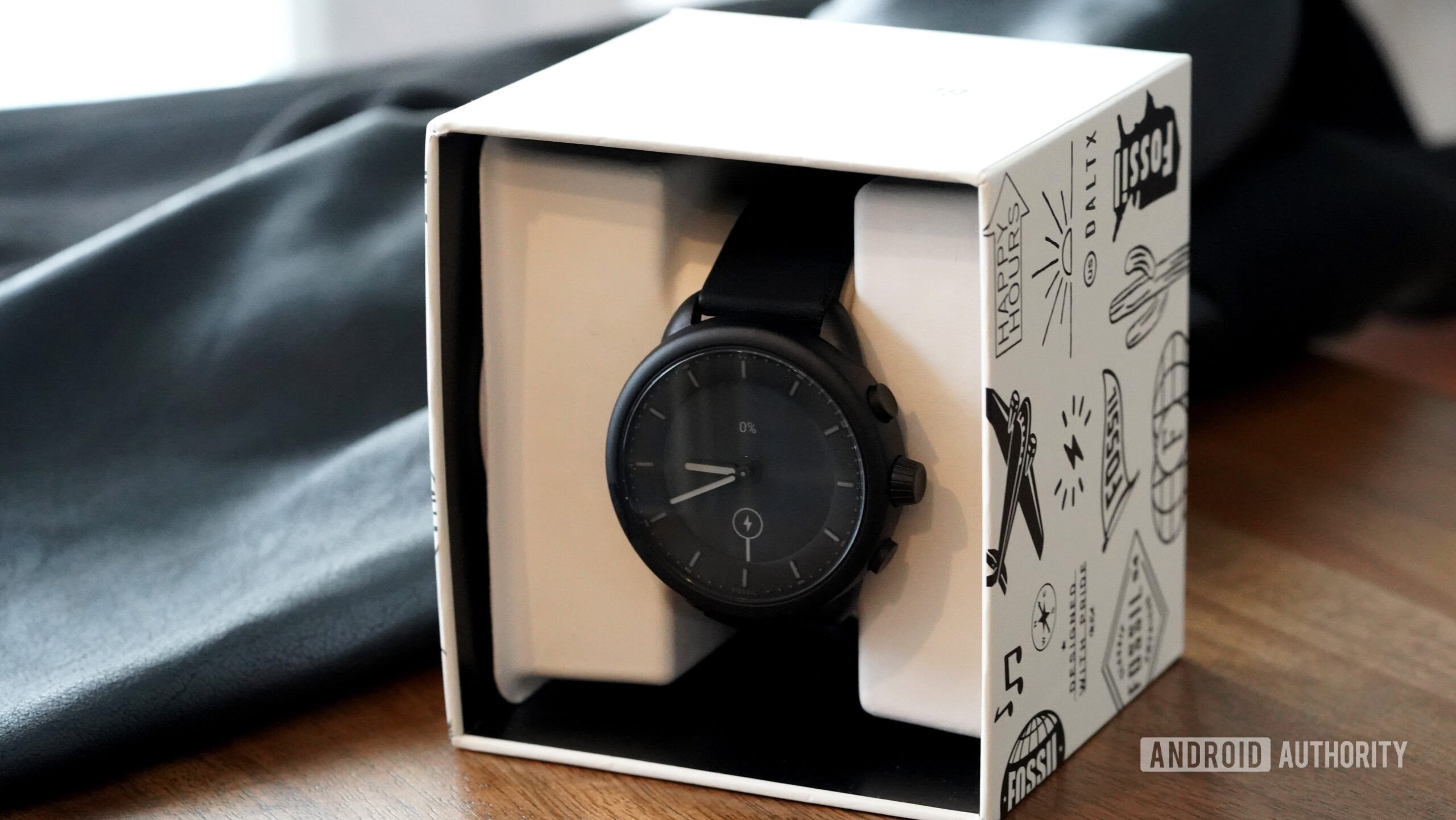 A Fossil Gen 6 Hybrid watch in its box rests on a wooden surface.