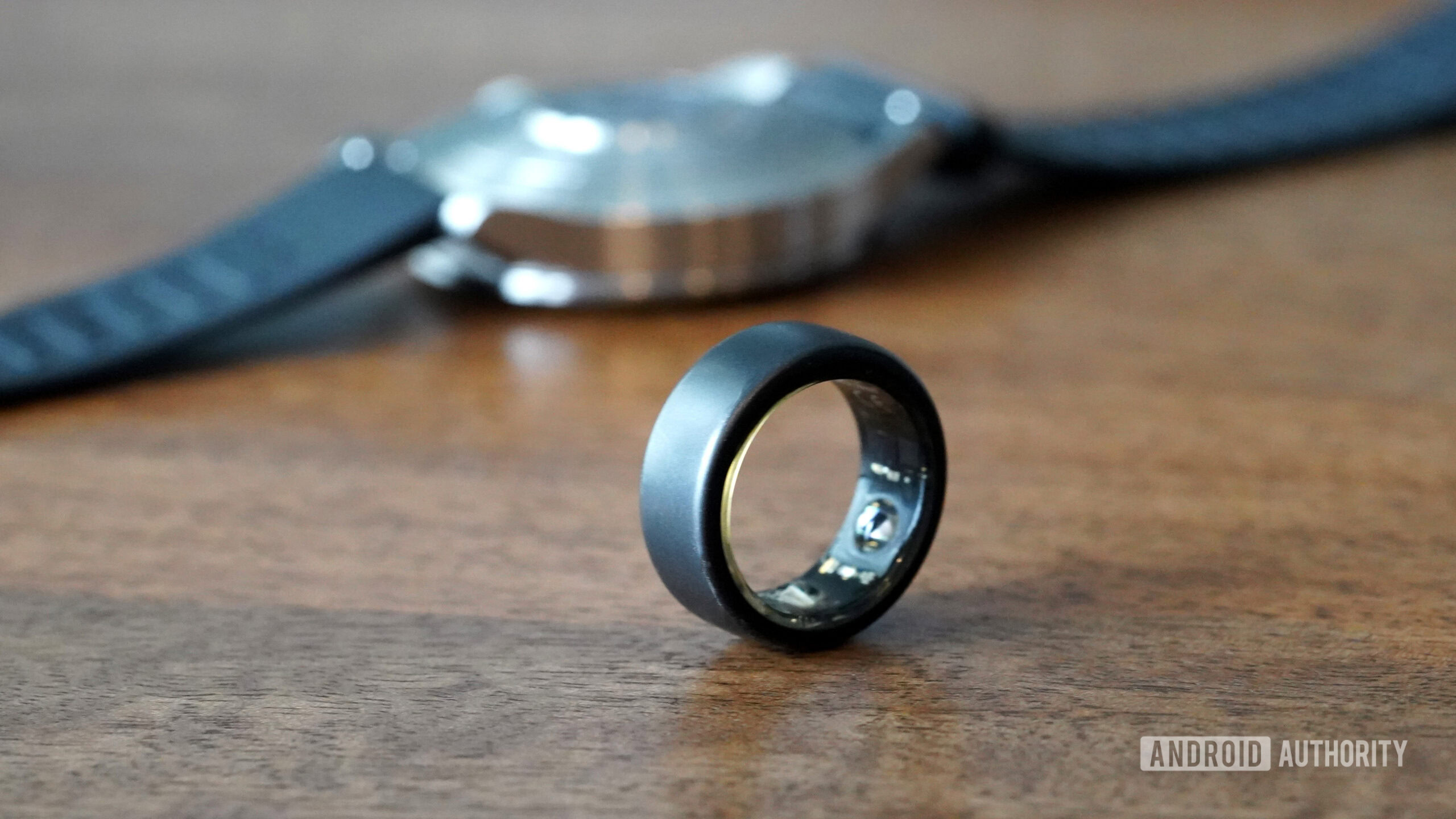 An Oura Ring 3 rests in front of a hybrid smartwatch.