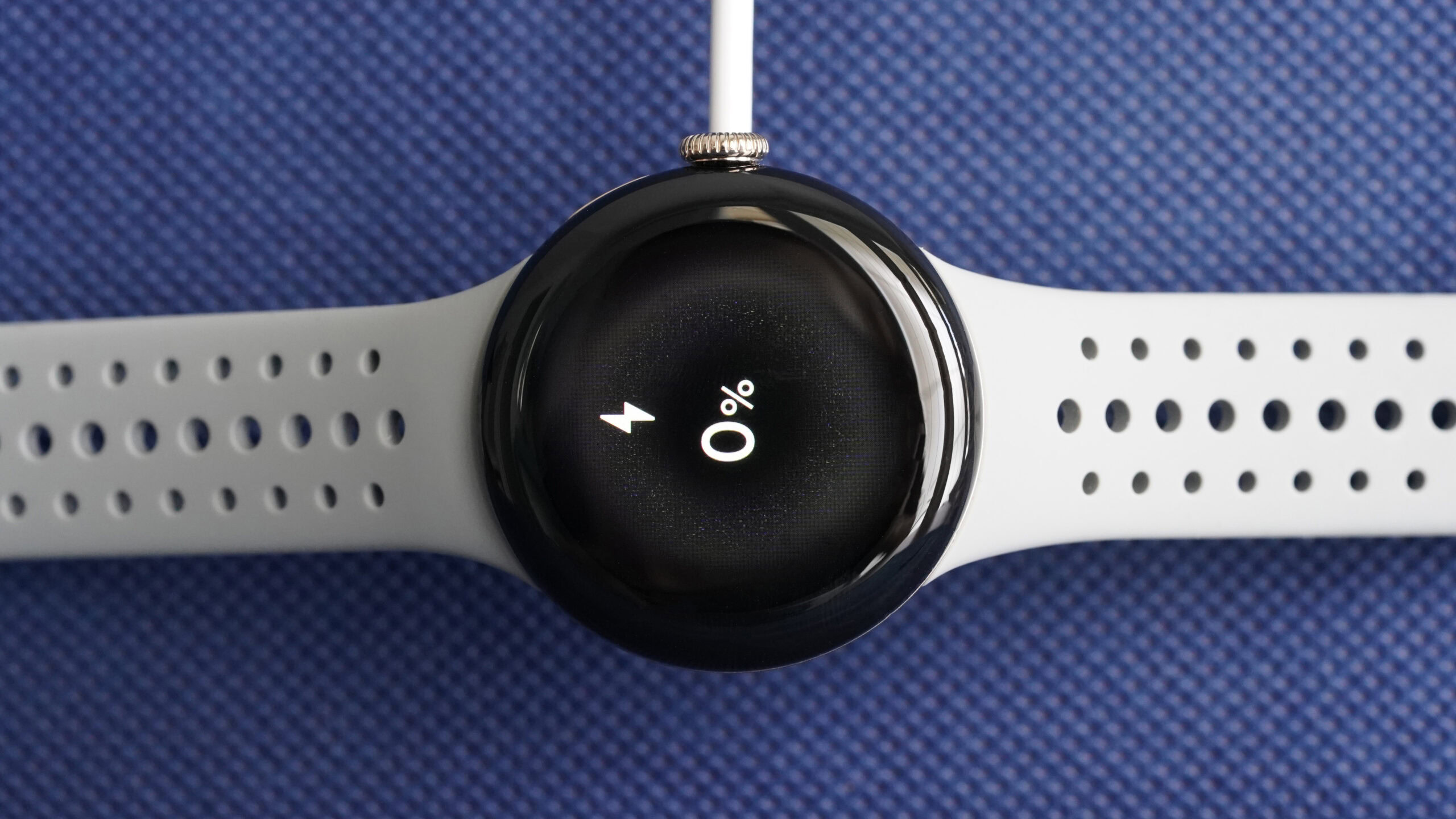 A charging Pixel Watch 2 displays the device's battery status at zero percent.