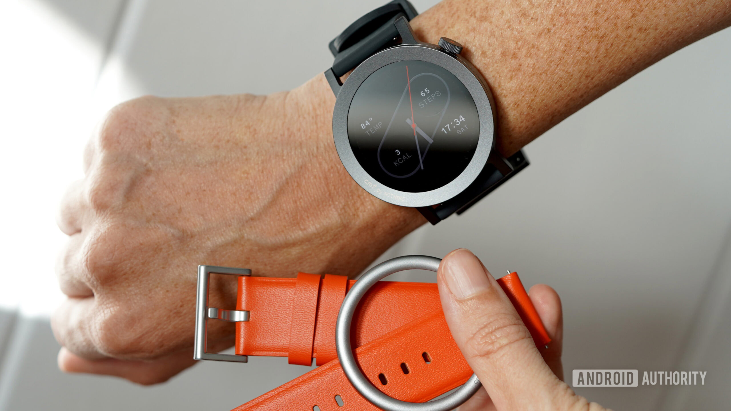 A CMF Watch user holds the device next to a set of alternatives bands and an alternative bezel.