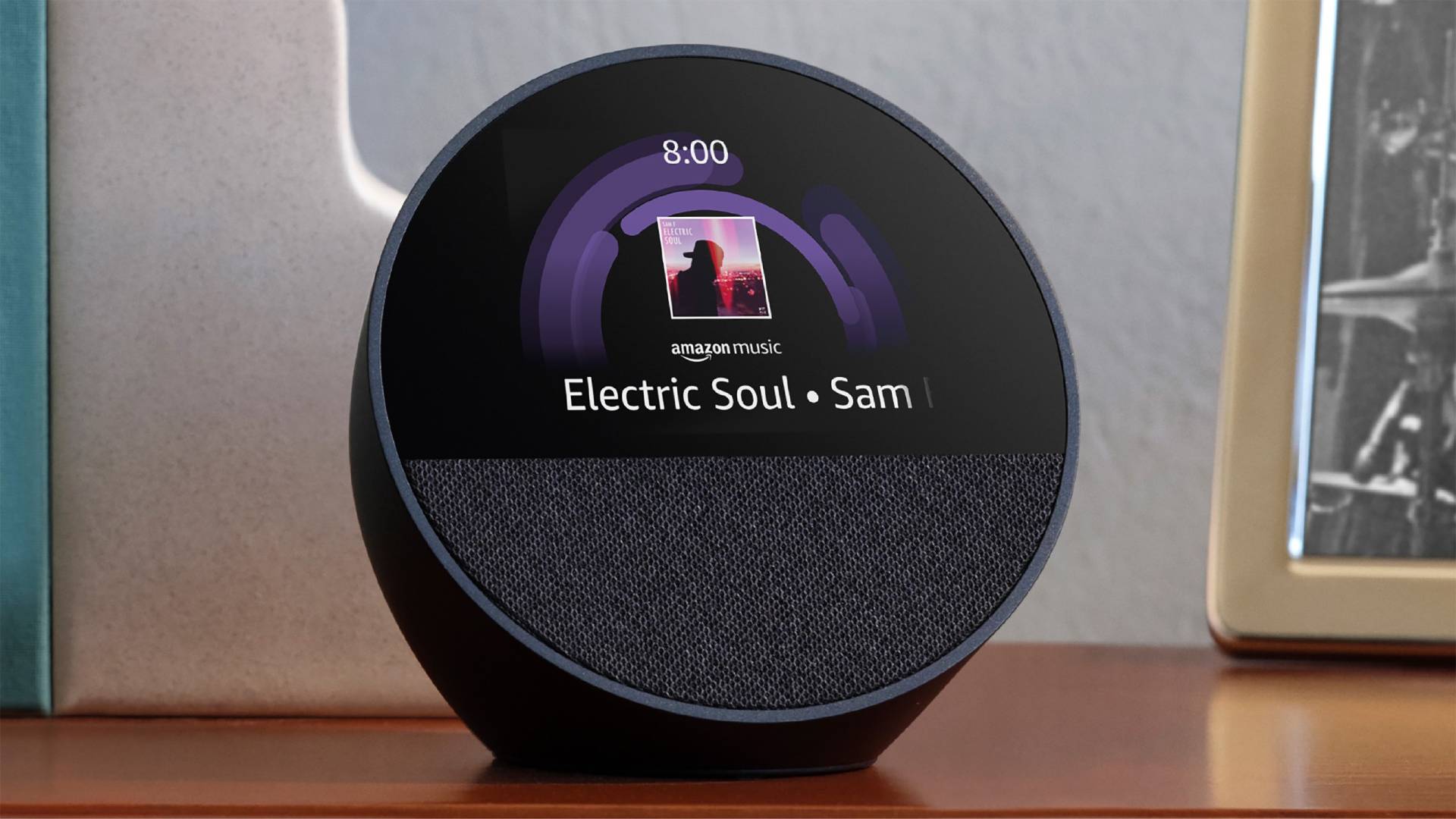 Black Echo Spot (2024) placed on a table with album art and time on the display.
