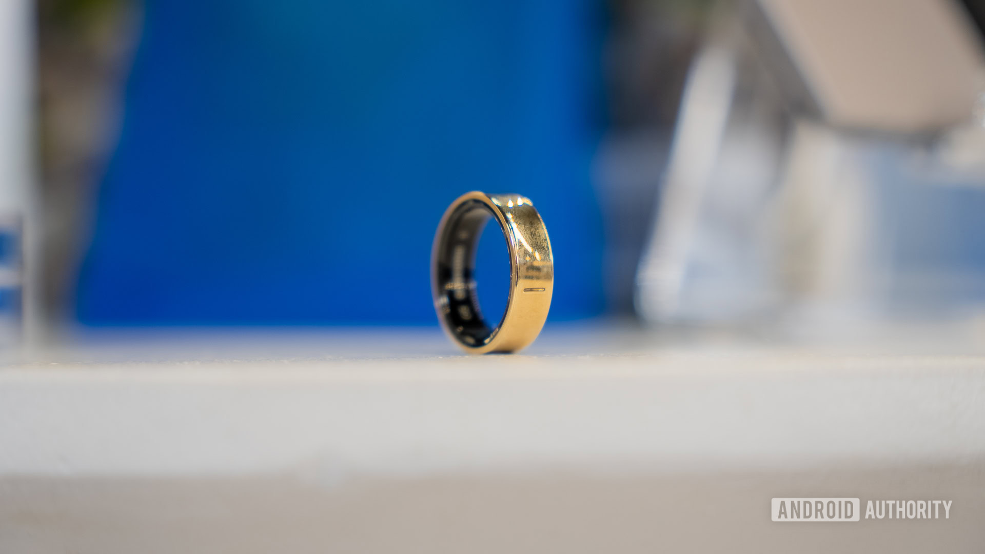 A Gold Titanium Samsung Galaxy Ring rests on a white surface.