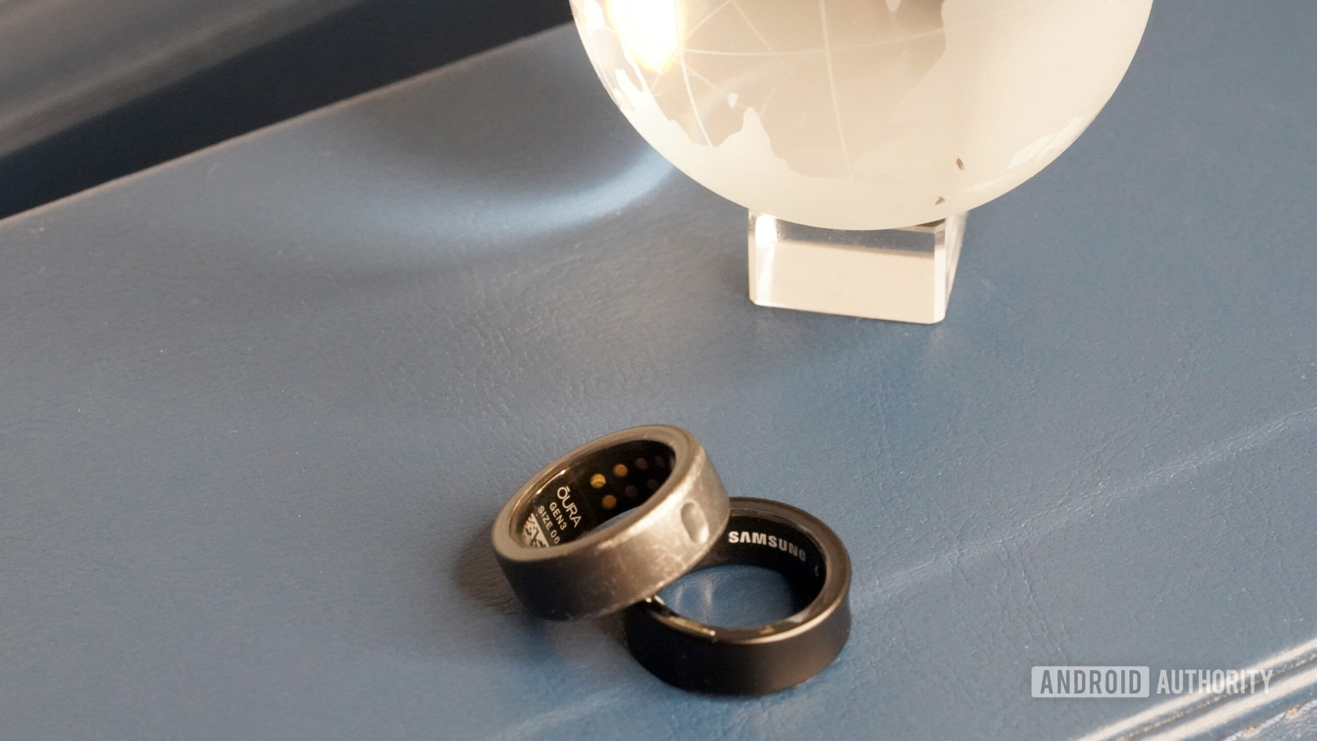 A Samsung Galaxy Ring rests alongside an Oura Ring 3 each highlighting its company label.