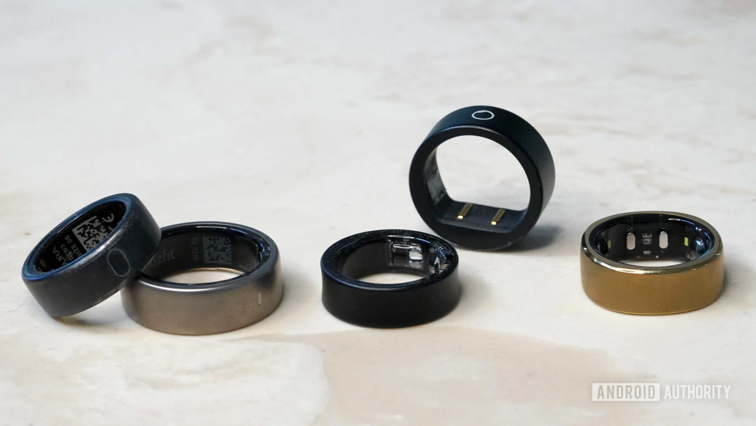 A variety of smart rings rest on a marble surface.