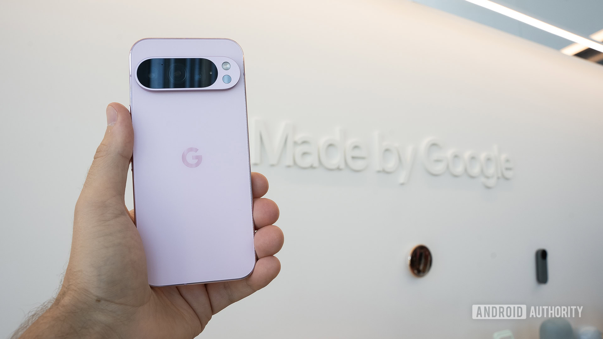 Google Pixel 9 Pro in Rose Quartz in man's left hand in front of Made by Google sign