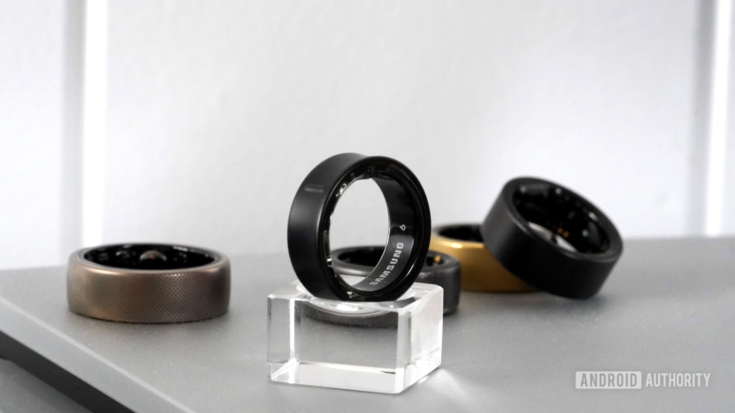 A Samsung Galaxy Ring rests on a small stand in front of alternative smart rings.