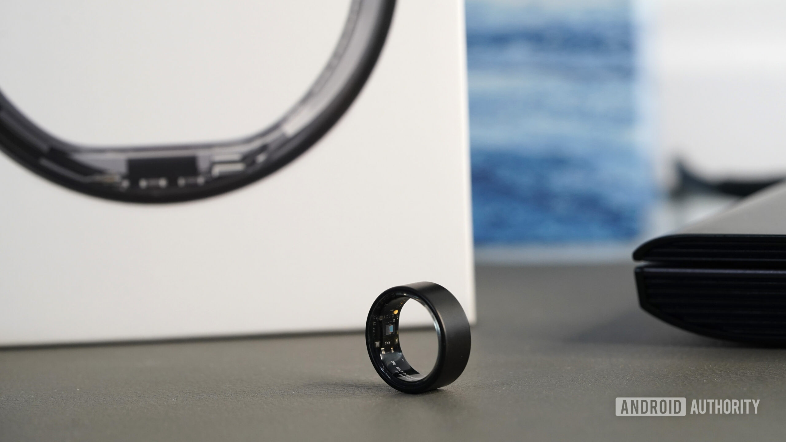 An Ultrahuman Ring Air rests on a desk in front of its packaging.