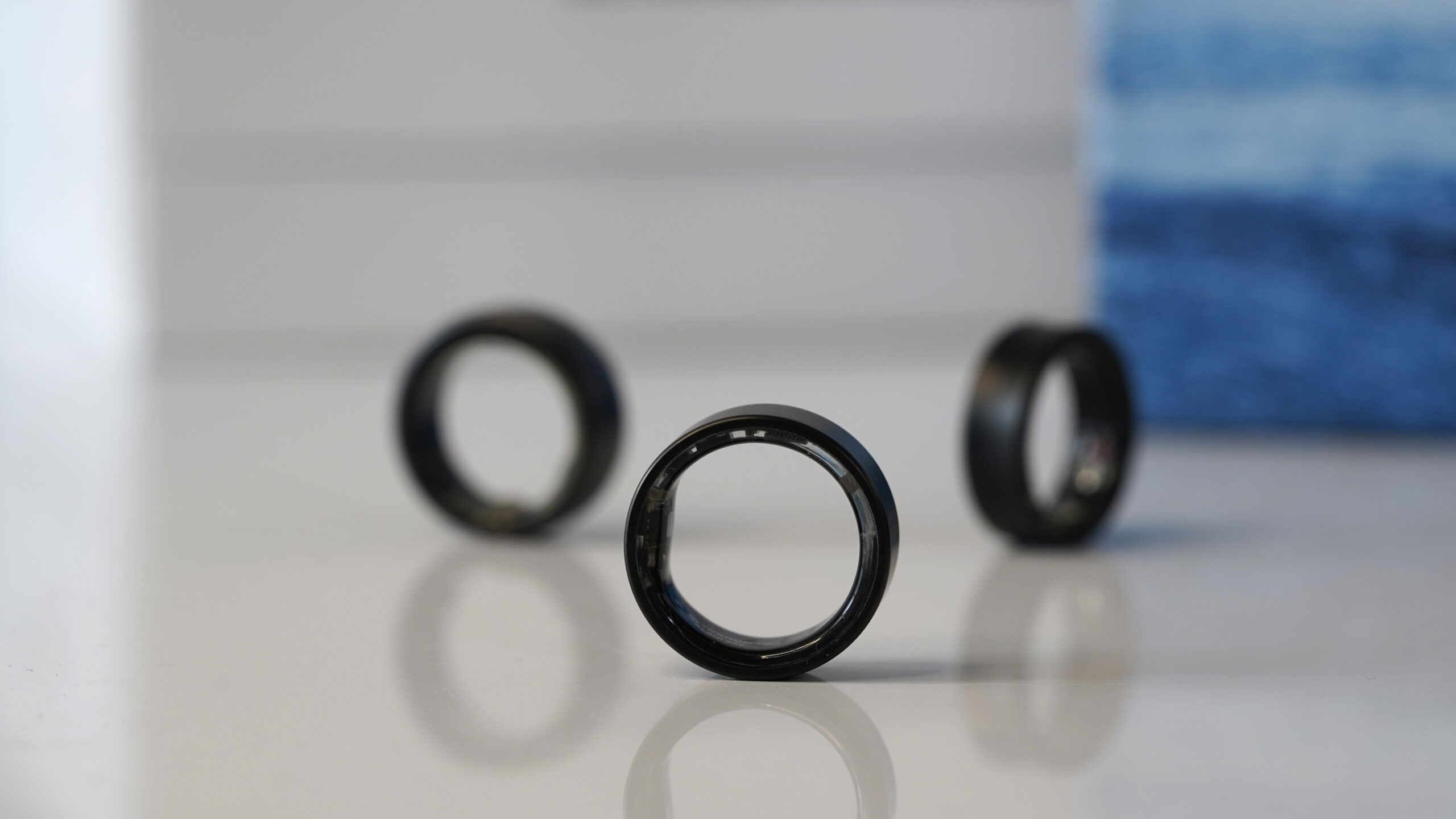 An Ultrahuman Ring Air stands on its edge in front of alternative devices.