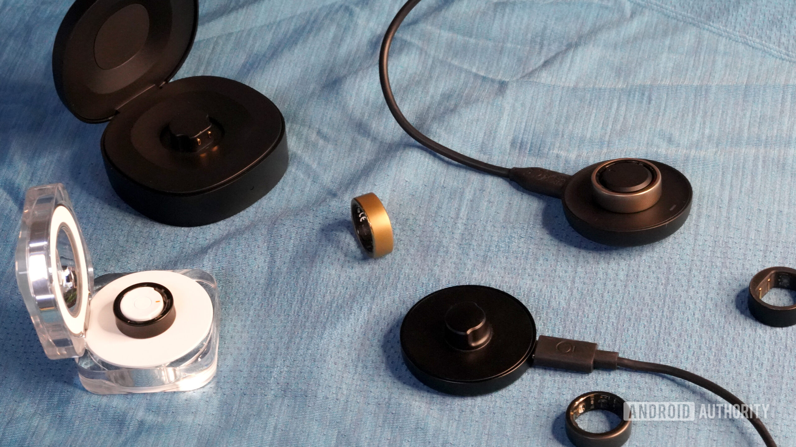 A variety of smart rings rest on their alongside their chargers