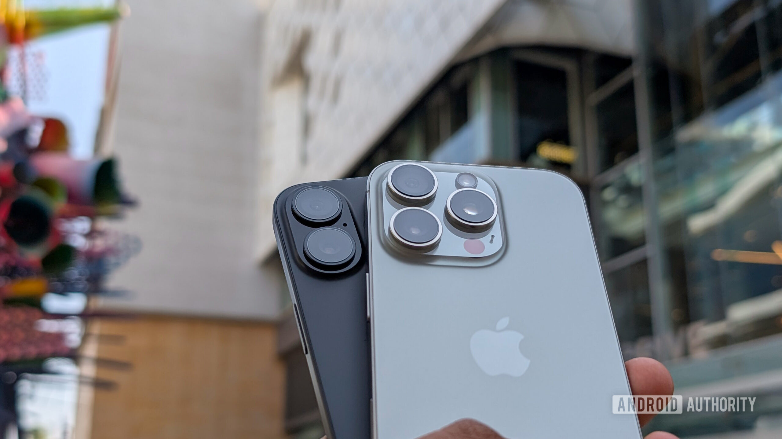 Apple iPhone 16 Plus in black color and iPhone 16 Pro in Natural Titanium color held out in hand, focusing on the camera