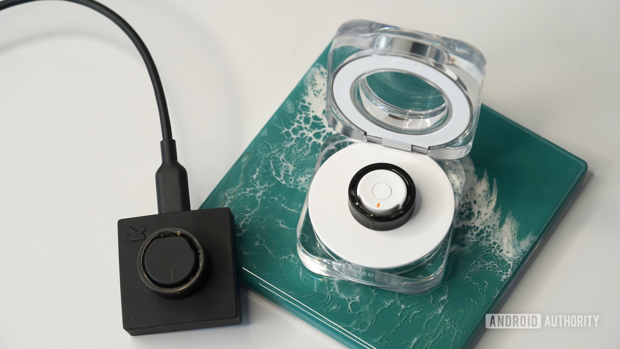 A Ultrahuman Ring Air charges alongside a Samsung Galaxy Ring also in its charging case.