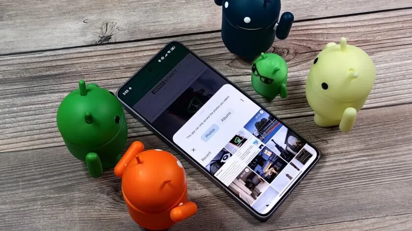 Cinco figuras de Android de diferentes colores rodean un smartphone, que muestra en su pantalla una interfaz de selección de fotos con opciones para elegir imágenes recientes o álbumes. La escena representa la funcionalidad de selección de fotos en dispositivos Android, destacando el acceso controlado a la galería multimedia del usuario.