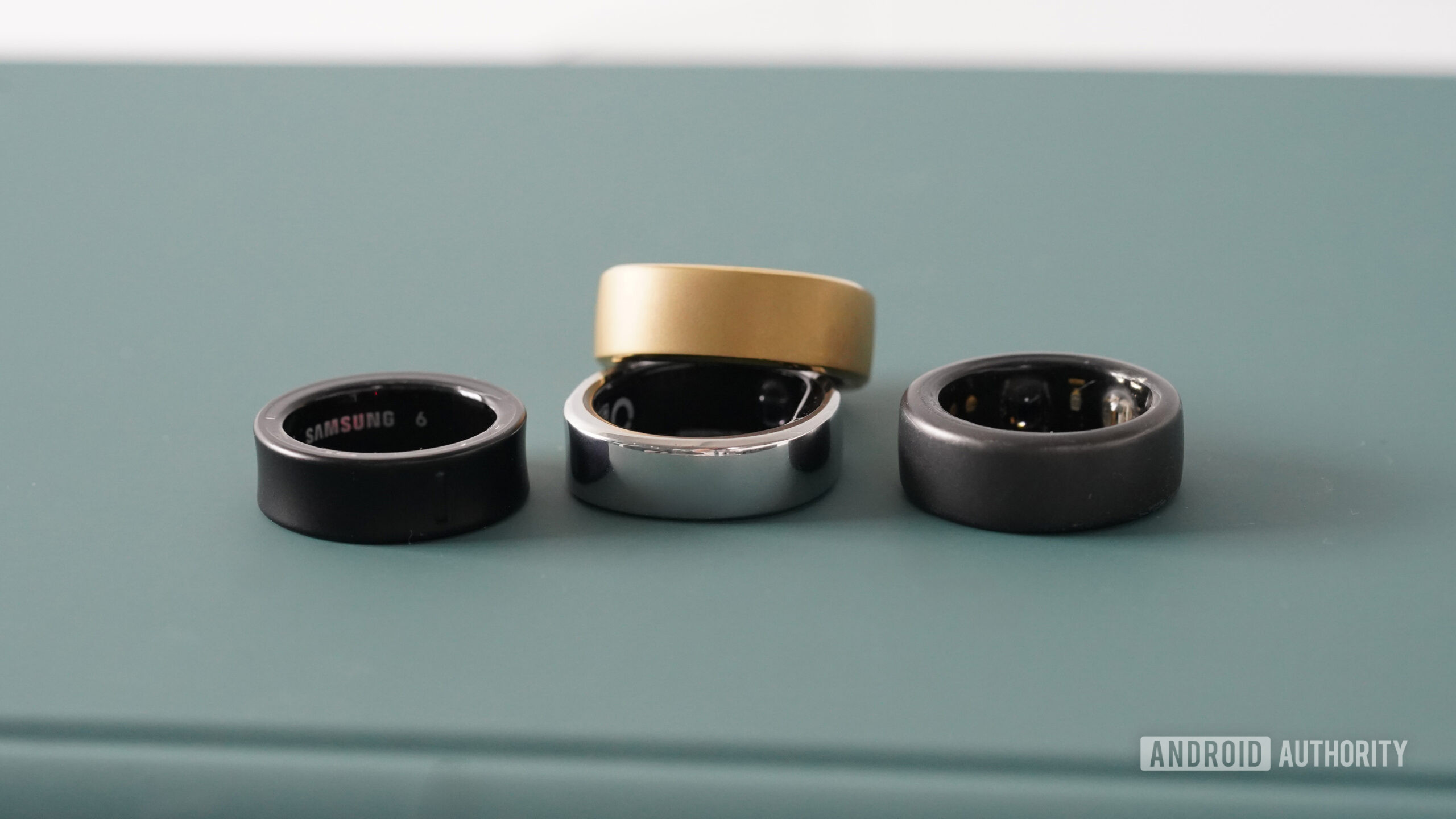 A RingConn Smart Ring Gen 2 rests alongside an Oura Ring, Galaxy Ring, and Gen 1 RingConn Smart Ring.