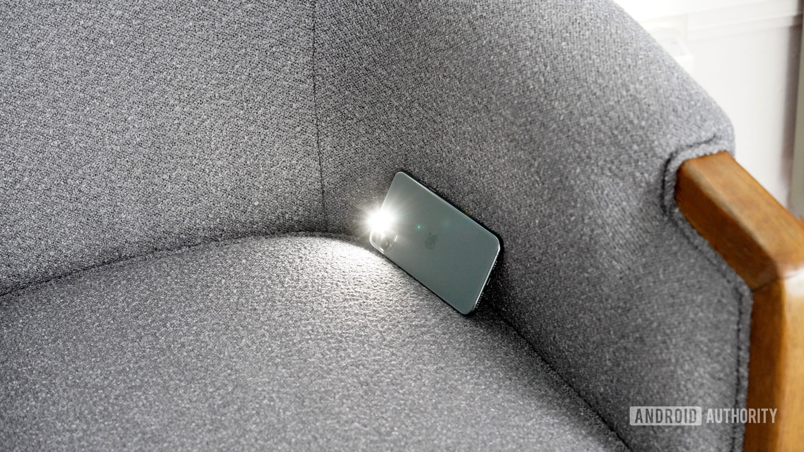 An iPhone rests lodged into a seat cushion with its flashlight on. 