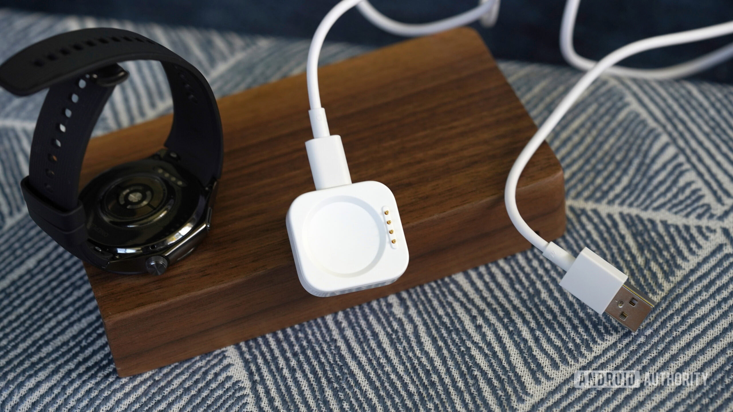 A OnePlus Watch 3 rests alongside its charger.